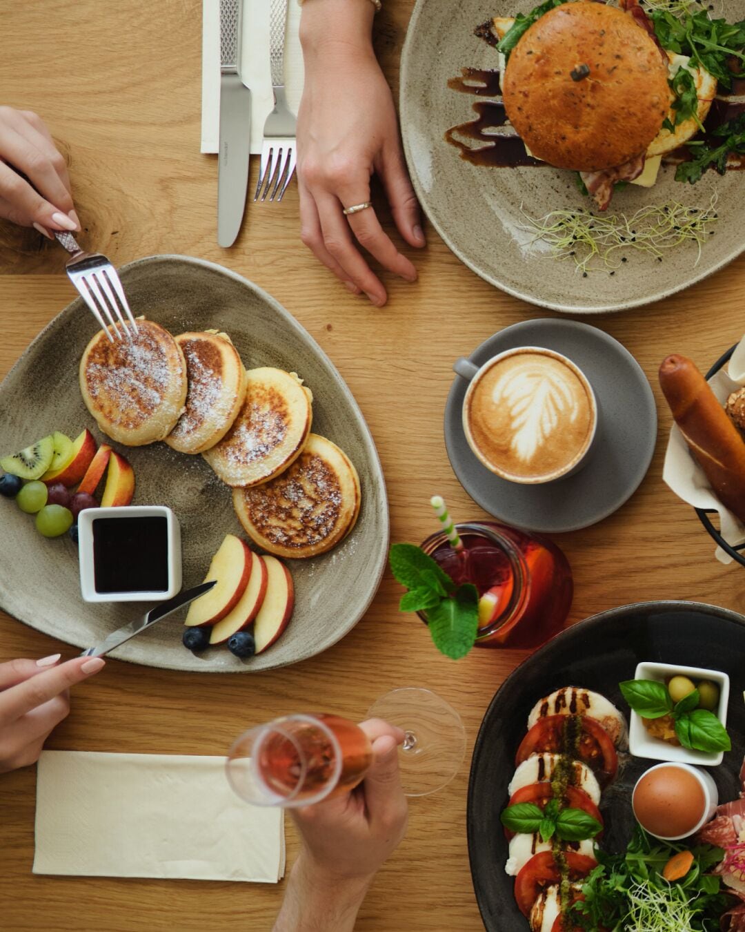 A breakfast setting with pancakes, fruit, coffee, and a variety of dishes on a wooden table.