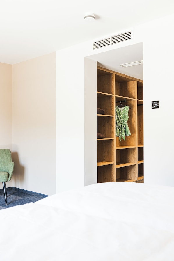 Une pièce avec une armoire en bois, une chaise verte et un lit avec une literie blanche.