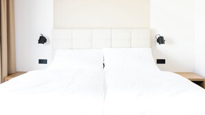 A double bed with white bedding, two bedside tables, and black wall-mounted lamps. - DAS DECKER (Paldau)