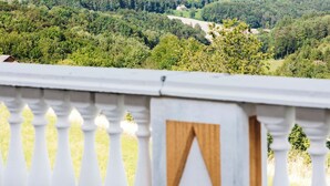 A balcony with a white balustrade overlooking a lush green landscape with trees and a distant view of a valley. - DAS DECKER (Paldau)