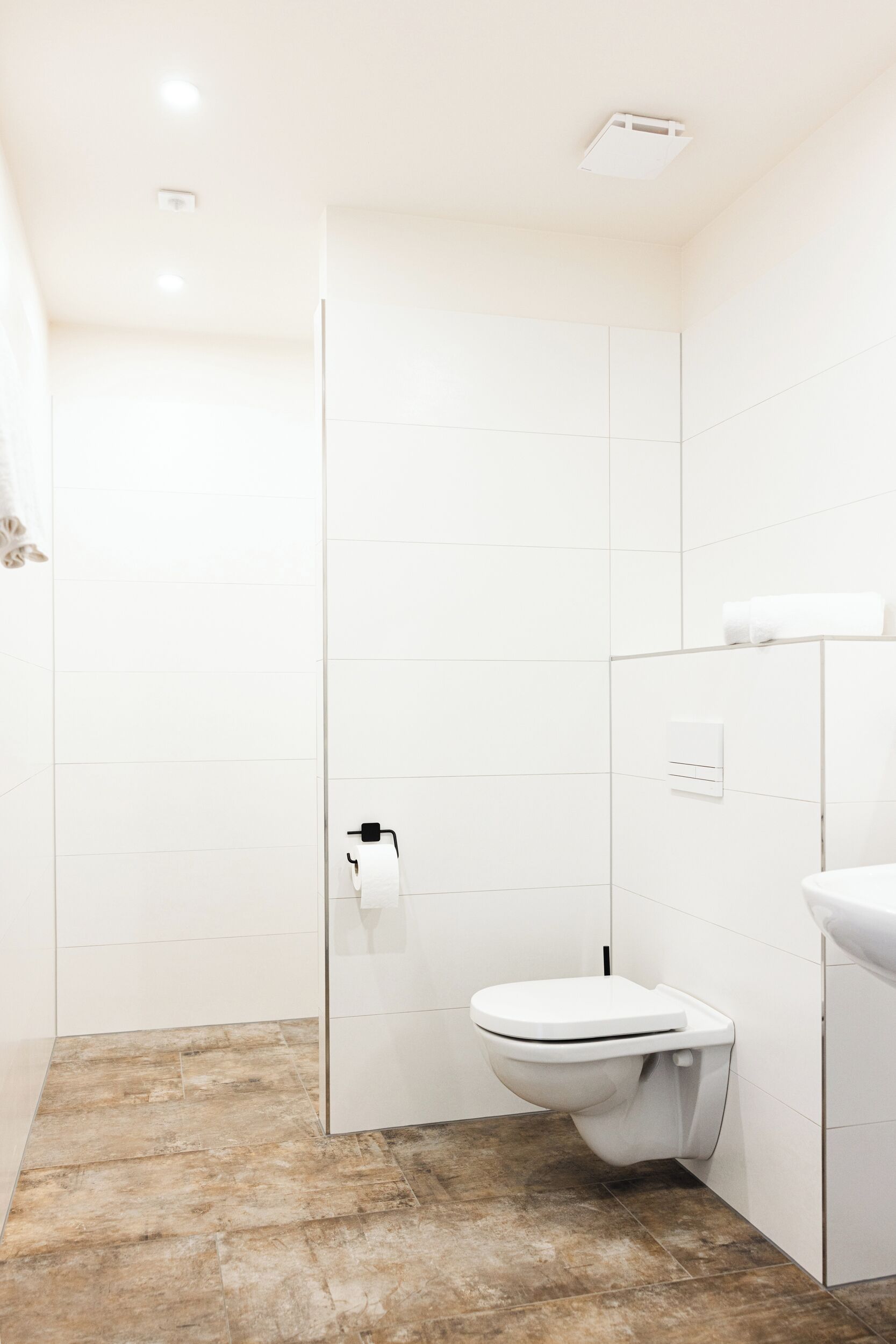 Ein modernes Badezimmer mit weißen Fliesen, Toilette, Duschbereich und Waschbecken.