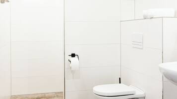 Ein modernes Badezimmer mit weißen Fliesen, Toilette, Duschbereich und Waschbecken.