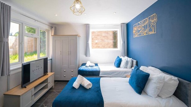 A modern hotel room with two beds, a TV, and a large window. - Cozy Garden Studio in St Albans (St Albans)