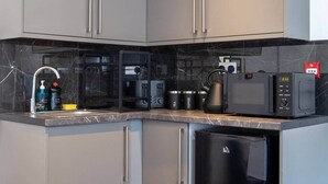 A modern kitchen with grey cabinets, a black countertop, a coffee machine, a kettle, and a microwave. - Cozy Garden Studio in St Albans (St Albans)
