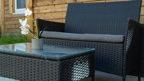 A wicker chair with a cushion, a glass table, and a potted plant with white flowers. - Cozy Garden Studio in St Albans (St Albans)