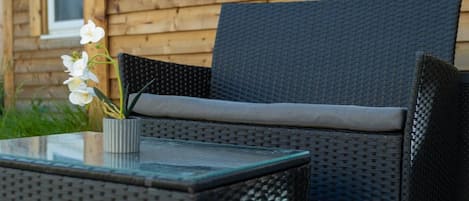 A wicker outdoor seating area with a glass table and a potted orchid.