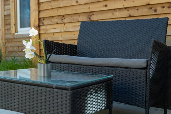 A wicker outdoor seating area with a glass table and a potted orchid.