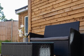A wooden exterior wall with a window, a wicker chair with a cushion, and a potted orchid. - Cosy Garden Studio l Free Parking, WiFi l Sleeps 3 (St Albans)