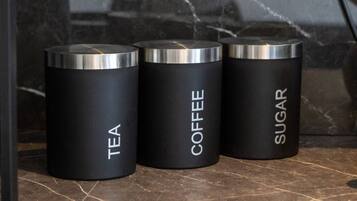 Three cylindrical containers labeled tea, coffee, and sugar on a marble surface.