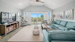 A spacious living room with a television, sofas, a coffee table, and a ceiling fan. - Coastal Aire - Gulf Front 3 bed, 4 bath! (Port St. Joe)