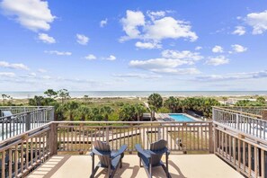 Ein Balkon mit zwei Adirondack-Stühlen mit Blick auf Pool und Strand.