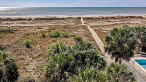 A beach view with a pathway leading to a pool area surrounded by palm trees and sparse vegetation. - Coastal Aire - Gulf Front 3 bed, 4 bath! (Port St. Joe)