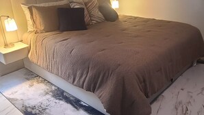Un dormitorio con cama, lámparas de noche, cabecero y una alfombra estampada.