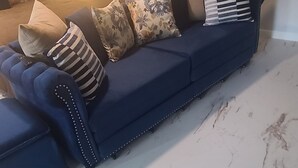 Un sofá azul oscuro con cojines estampados de flores y rayas, un reposabrazos capitonado y un suelo con diseño de mármol.