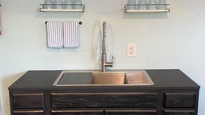 Una cocina de madera oscura con un lavabo, dos repisas encima del lavabo con vasos, y una toalla colgada en la pared.