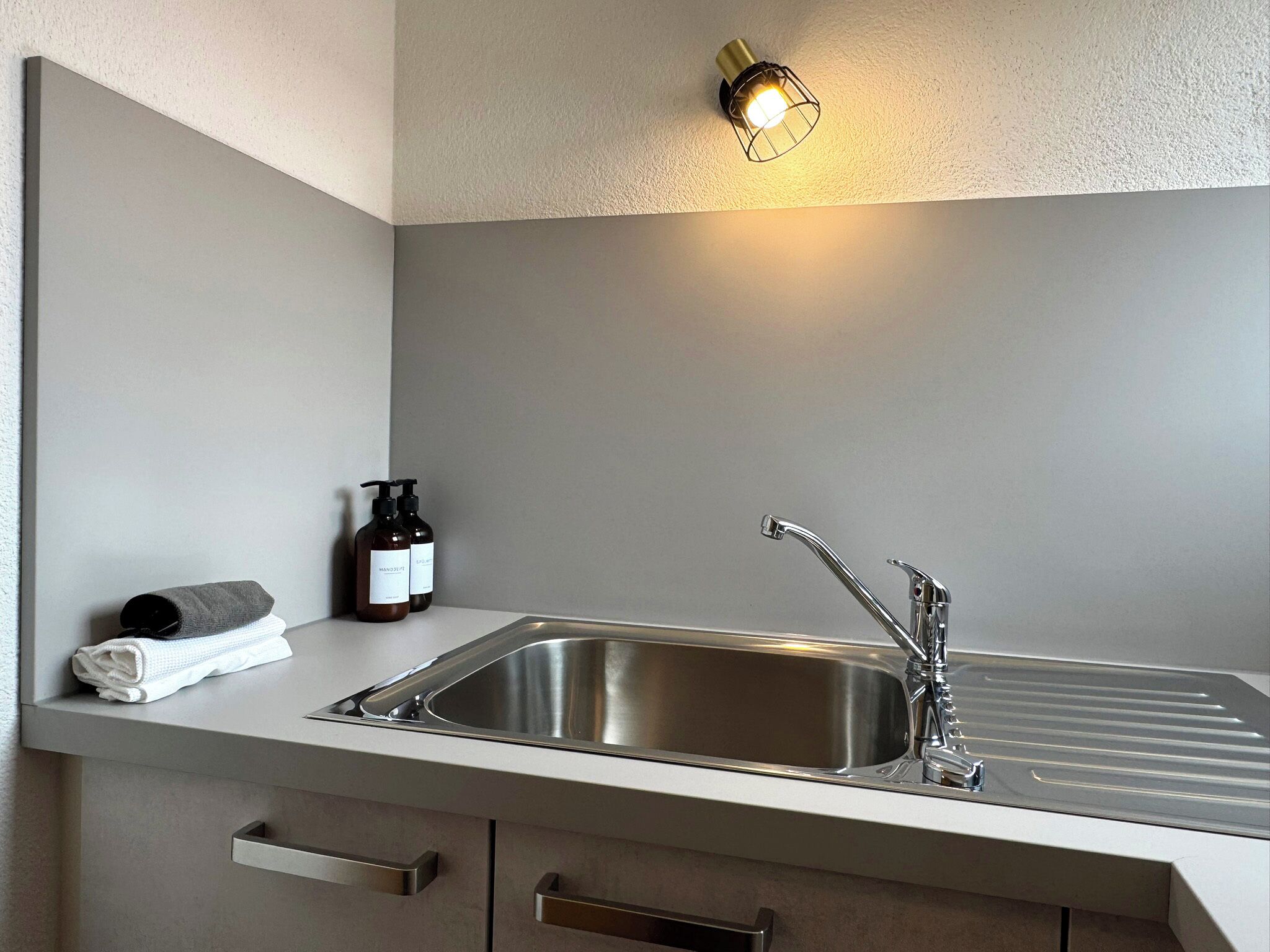 Een moderne keuken met een RVS spoelbak, een handdoek en twee flessen handzeep.