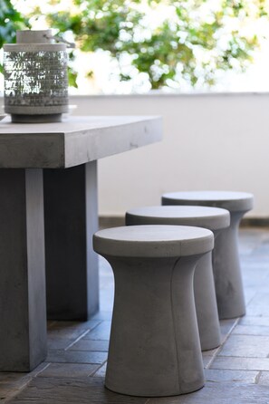 A concrete table and stools with a textured glass container on top.