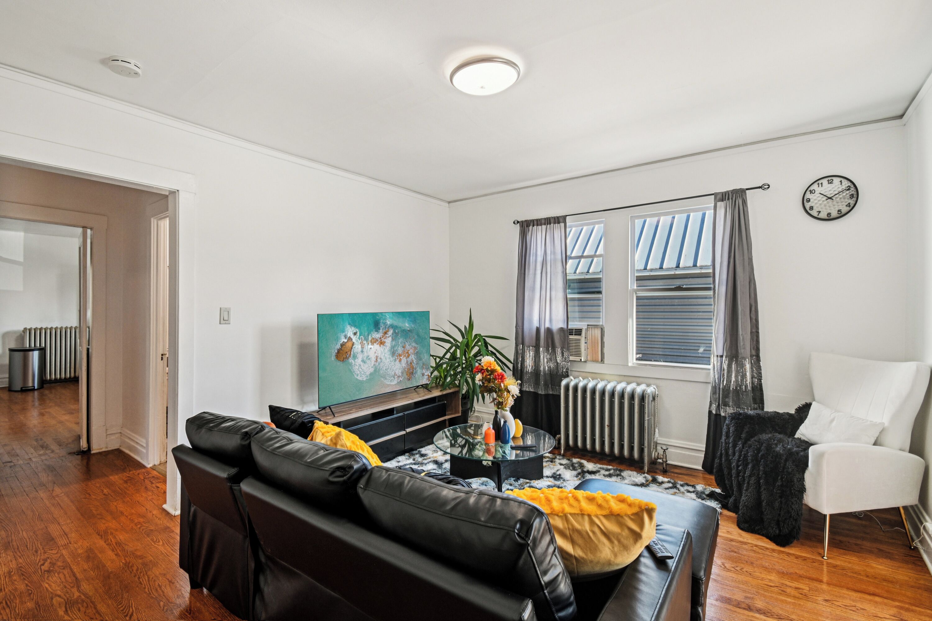 A modern living room with a black leather sofa, a glass coffee table, and a painting on the wall.