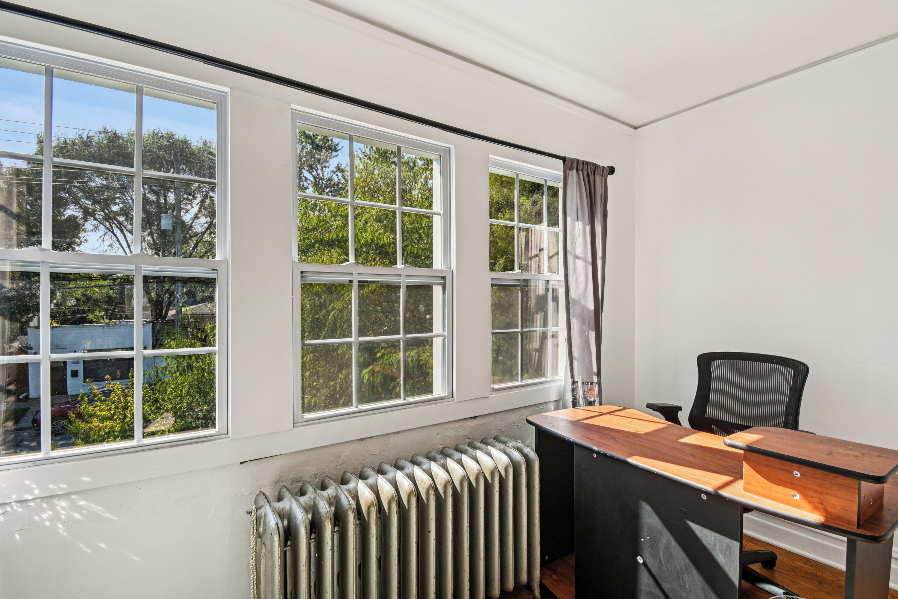 A room with a large window, a radiator, and a desk with a chair.