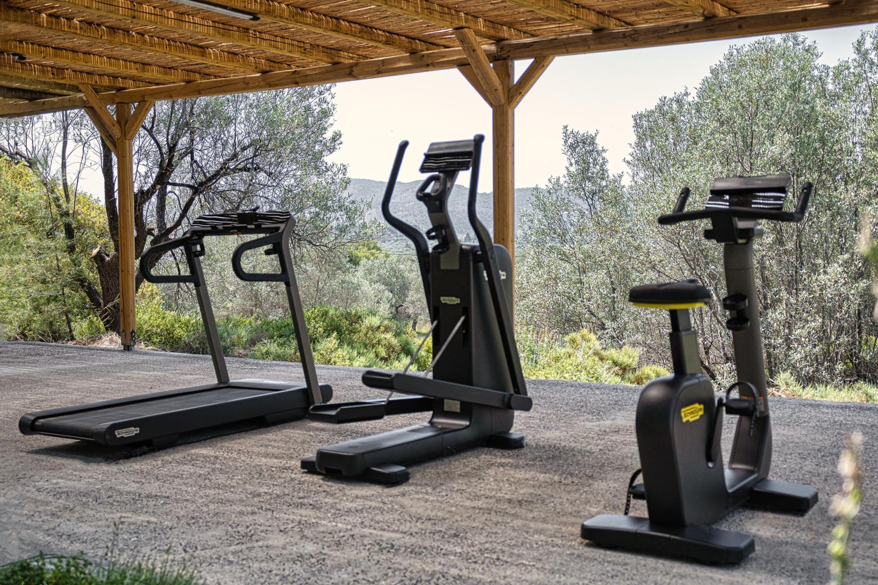 A covered outdoor area with exercise equipment including a treadmill, an elliptical, and a stationary bike.