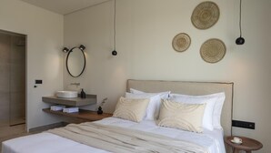 A modern bedroom with a large bed, a bedside table, a round mirror, and a wall-mounted shelf with a sink.