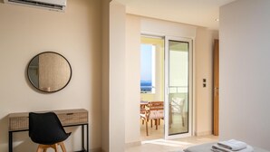 A hotel room with a desk, a chair, two beds, a round mirror, and a sliding glass door leading to a balcony with outdoor furniture. - Sunset View Paradisi Villa (Rhodes)