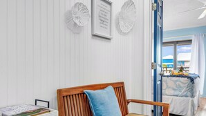 A room with a wooden bench, a white dresser, and a bed with a blue and white bedspread. - 1-minute walk to beach, Townhome in Welcoming Old Florida Saint George Island! (Saint George Island)