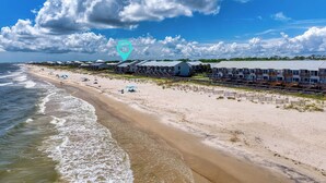 A beach resort with multiple bungalow-style buildings, a sandy beach, and ocean waves. - 1-minute walk to beach, Townhome in Welcoming Old Florida Saint George Island! (Saint George Island)