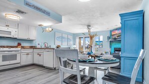 A modern kitchen with white cabinets, a dining area with a round table, and a blue accent wall. - 1-minute walk to beach, Townhome in Welcoming Old Florida Saint George Island! (Saint George Island)