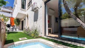 A swimming pool with a tiled edge, a patio with a table and chairs, and a view of a building with a large window and a stone feature. - Stunning Views, Walk to Beach, Heated Splash Pool - Iparadesi (Cape Town)