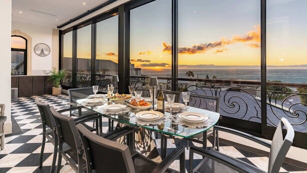 A dining table set for four with a view of the sunset over the ocean. - Stunning Views, Walk to Beach, Heated Splash Pool - Iparadesi (Cape Town)