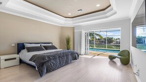 A bedroom with a bed, a nightstand, a potted plant, a view of a pool, and a chair. - Tranquil Island Retreat with Modern Comforts (Marco Island)