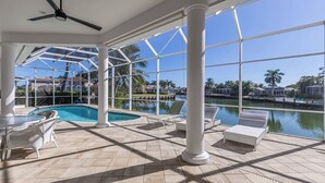 A pool area with clear views of a marina and palm trees, surrounded by white columns and lounge chairs. - Tranquil Island Retreat with Modern Comforts (Marco Island)