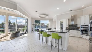 A spacious kitchen with a large island, white cabinetry, and a view of a pool and outdoor area. - Tranquil Island Retreat with Modern Comforts (Marco Island)
