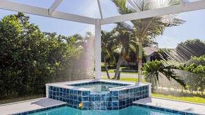 Uma banheira de hidromassagem com revestimento de azulejos, cercada por uma estrutura de pérgola branca, com um cenário de vegetação exuberante e área residencial.