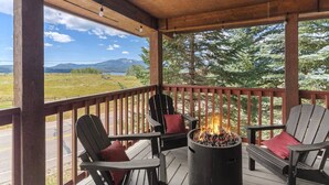 Eine überdachte Terrasse mit Adirondack-Stühlen, einer Feuerstelle und Blick auf eine gebirgige Landschaft.