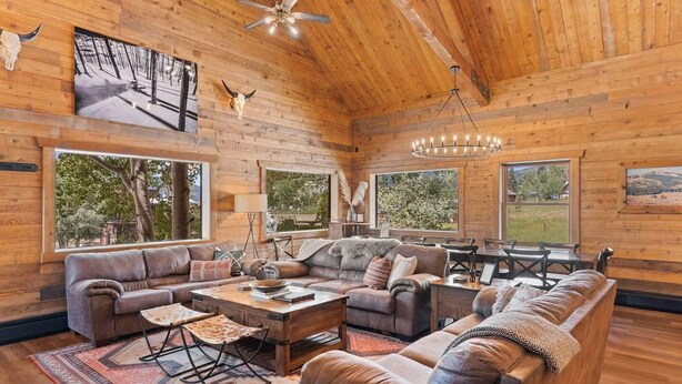 Ein geräumiges Wohnzimmer mit einer großen Holzbalkendecke, Ledersofas, einem Couchtisch und einer Chandelier.