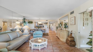 A spacious living room with a beige sofa, a glass coffee table, and a dining area with a table and chairs.