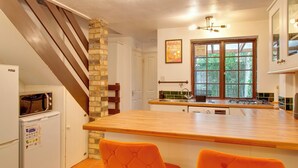 A kitchen with a wooden island, two orange chairs, a brick column, and a window with a view of greenery. - Stylish Victorian Terrace in Central Cambridge | Pass the Keys (Cambridge)