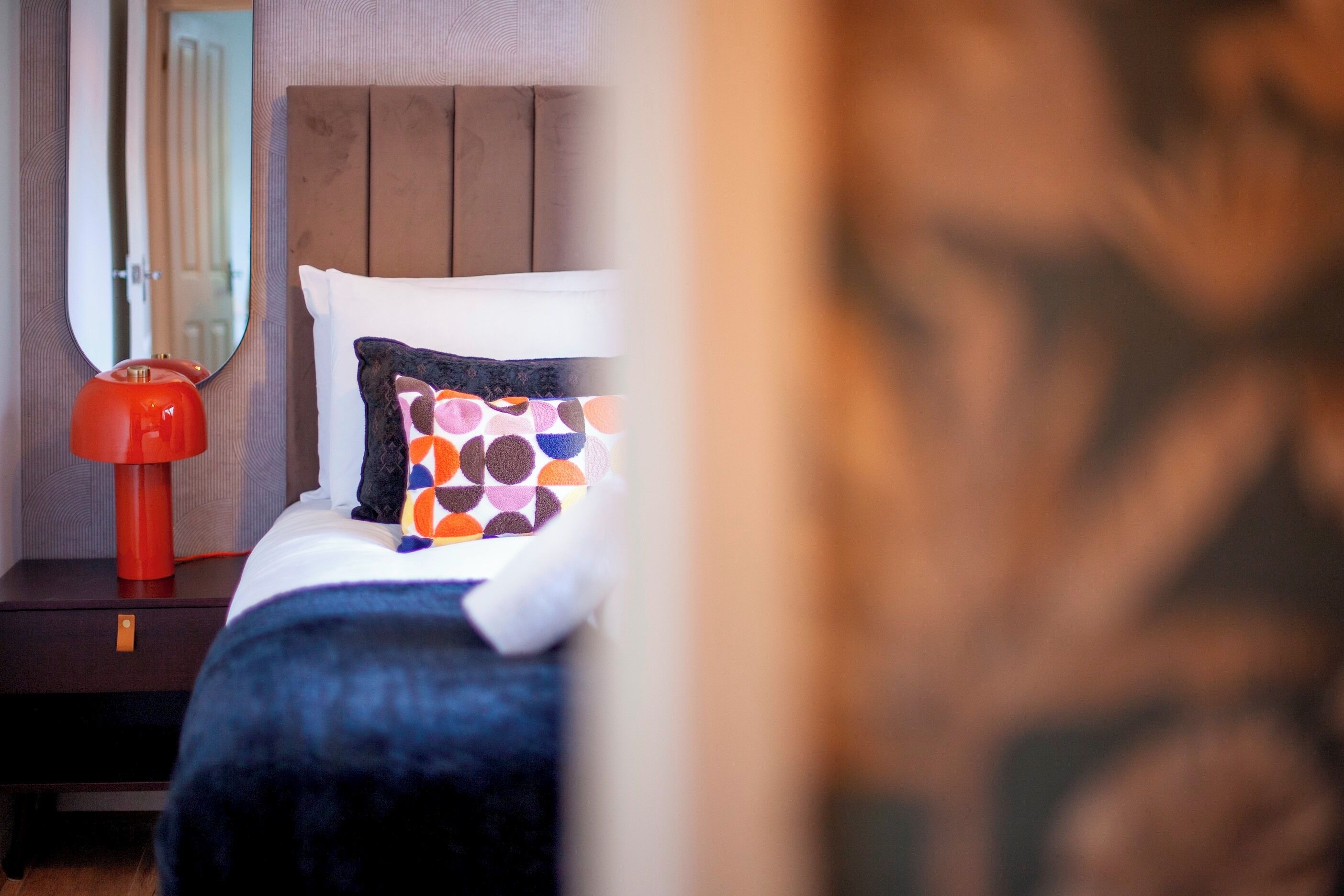 Un dormitorio con cama, mesita de noche, lámpara roja y espejo.