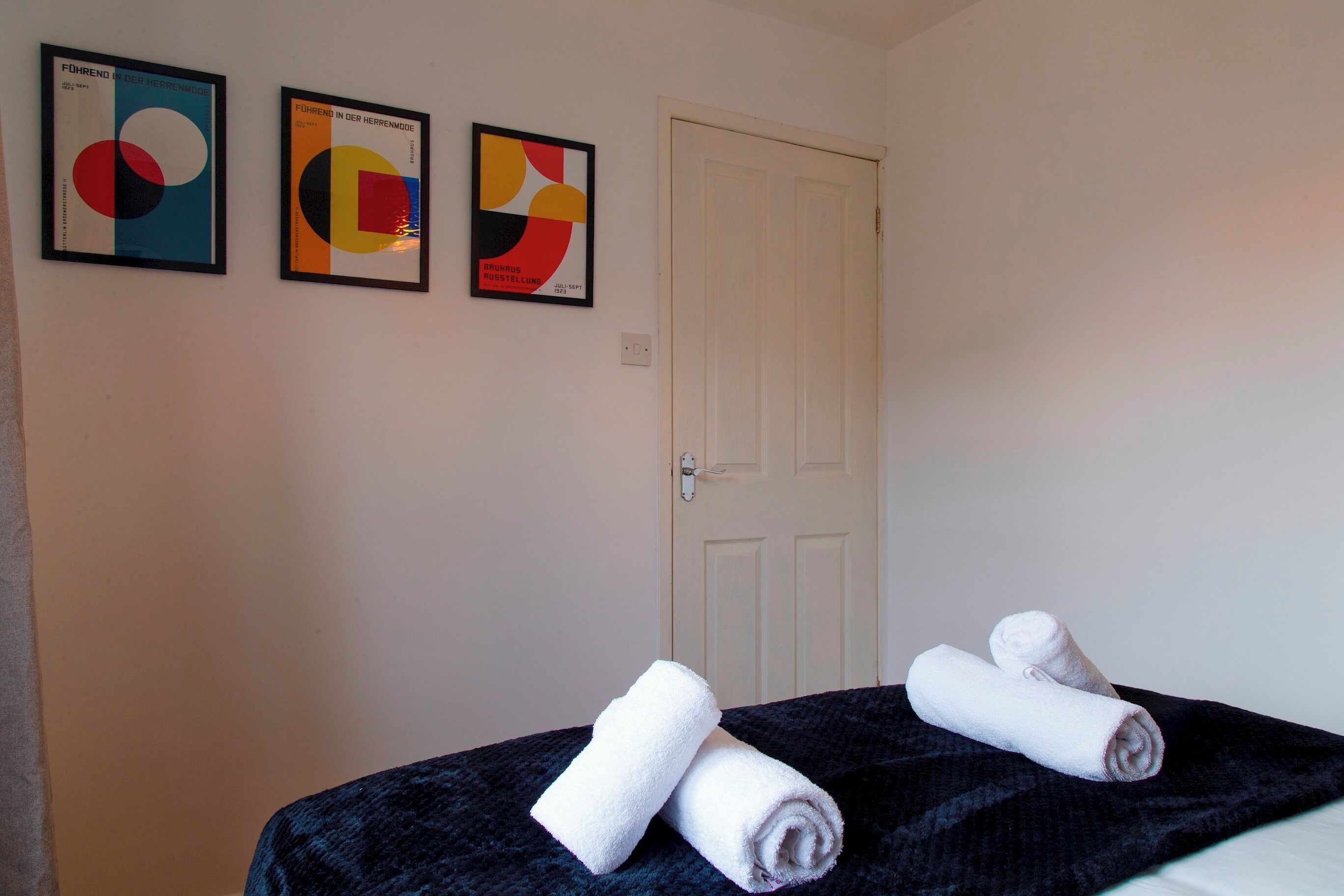 A room with two framed abstract artworks on the wall, a closed door, and two rolled towels on a bed.
