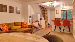 A cozy living room with a sofa, a wooden coffee table, and a kitchen area with a bar and stools. - Stylish Victorian Terrace in Central Cambridge | Pass the Keys (Cambridge)
