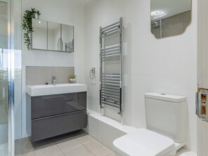 Une salle de bain moderne avec une douche à parois de verre, un lavabo blanc avec un miroir au-dessus, un porte-serviettes et des toilettes.