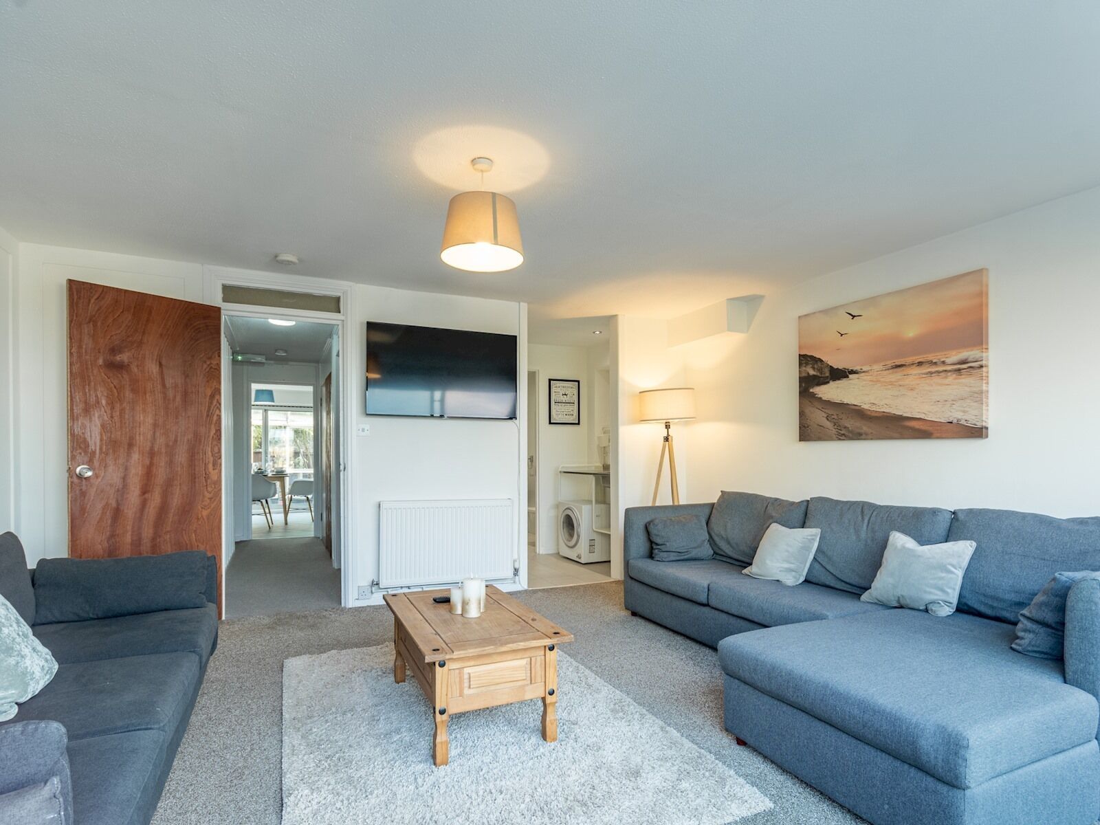 A modern living room with a grey sofa, a wooden coffee table, and a large painting of a beach scene.