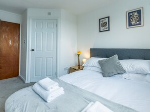 Une chambre d’hôtel avec un lit, une table de chevet, un vase de fleurs et deux tableaux encadrés au mur.