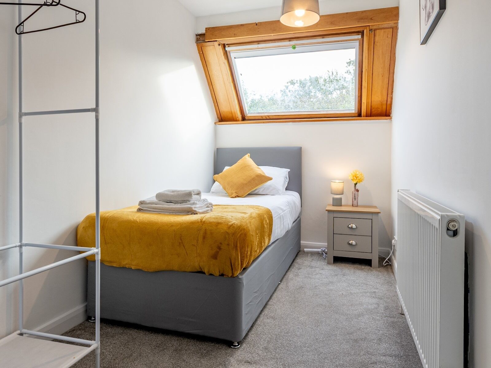 Une chambre à coucher comprenant un lit, une table de chevet, un radiateur, une fenêtre et un luminaire suspendu.