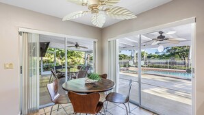 A spacious room with a round table and chairs, large sliding glass doors leading to an outdoor area with a pool and greenery. - Unwind in Paradise on Marco Island (Marco Island)