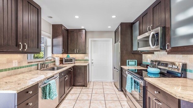 A modern kitchen with dark wood cabinets, a stainless steel refrigerator, a microwave, a stove, and a sink. - Unwind in Paradise on Marco Island (Marco Island)