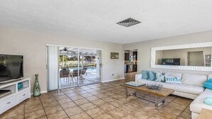 A living room with a TV, a coffee table, and a sofa. There is a sliding glass door leading to a pool area. - Unwind in Paradise on Marco Island (Marco Island)
