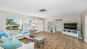 A living room with a sofa, coffee table, TV, and a view of palm trees through the window. - Unwind in Paradise on Marco Island (Marco Island)